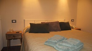 Una cama bien hecha con cabecera, dos almohadas y una pila de toallas dobladas.