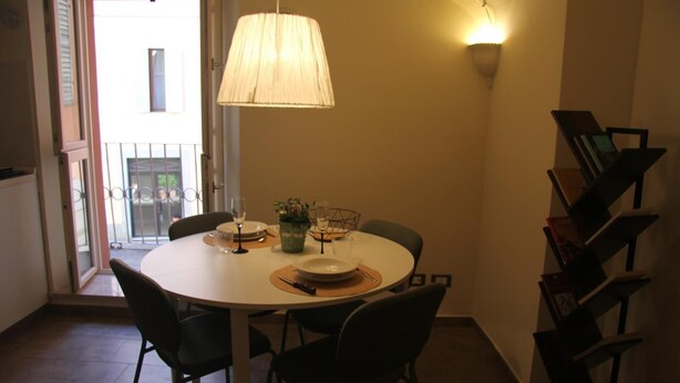 Un comedor con una mesa redonda, sillas, una lámpara colgante, una planta pequeña y una estantería.