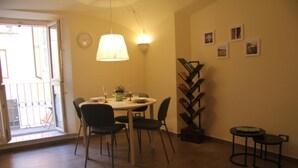 Comedor con mesa redonda, cuatro sillas, una lámpara colgante, una estantería y una pequeña mesa con un taburete.