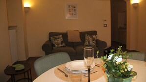 Comedor con una mesa dispuesta para dos, un sofá al fondo y una lámpara fijada a la pared.