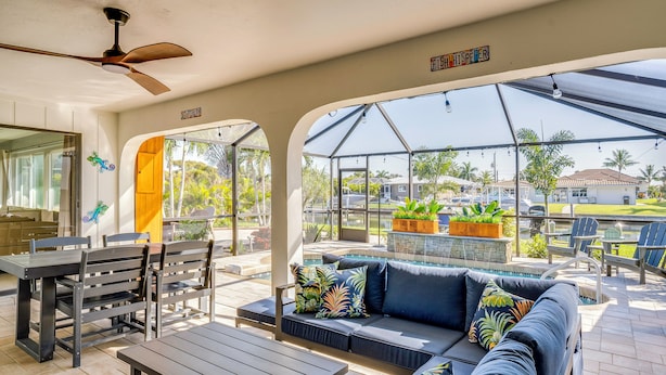 Eine überdachte Terrasse mit Deckenventilator, einer Couch mit tropischen Kissen, einem Esstisch und Stühlen.