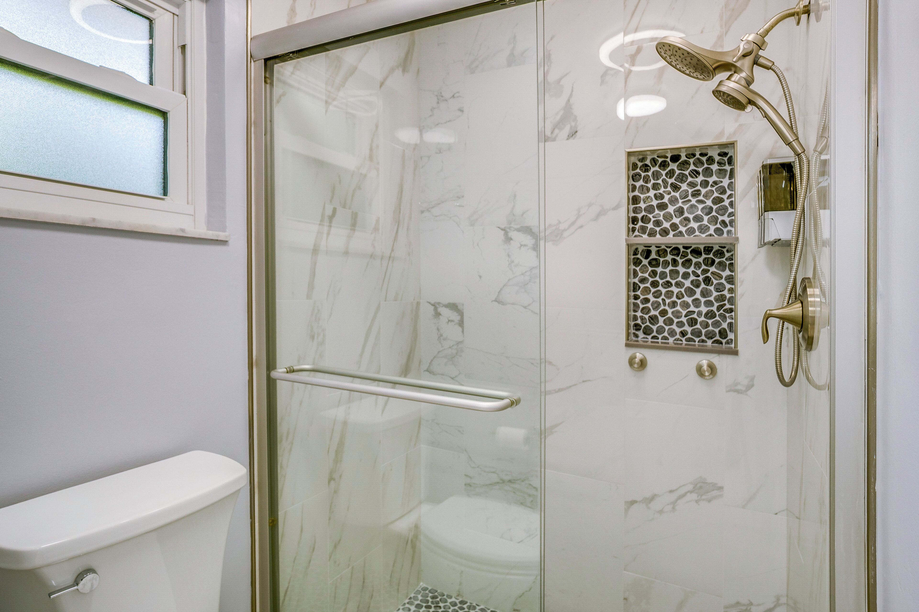 A bathroom with a glass-enclosed shower, a toilet, and a window with frosted glass.