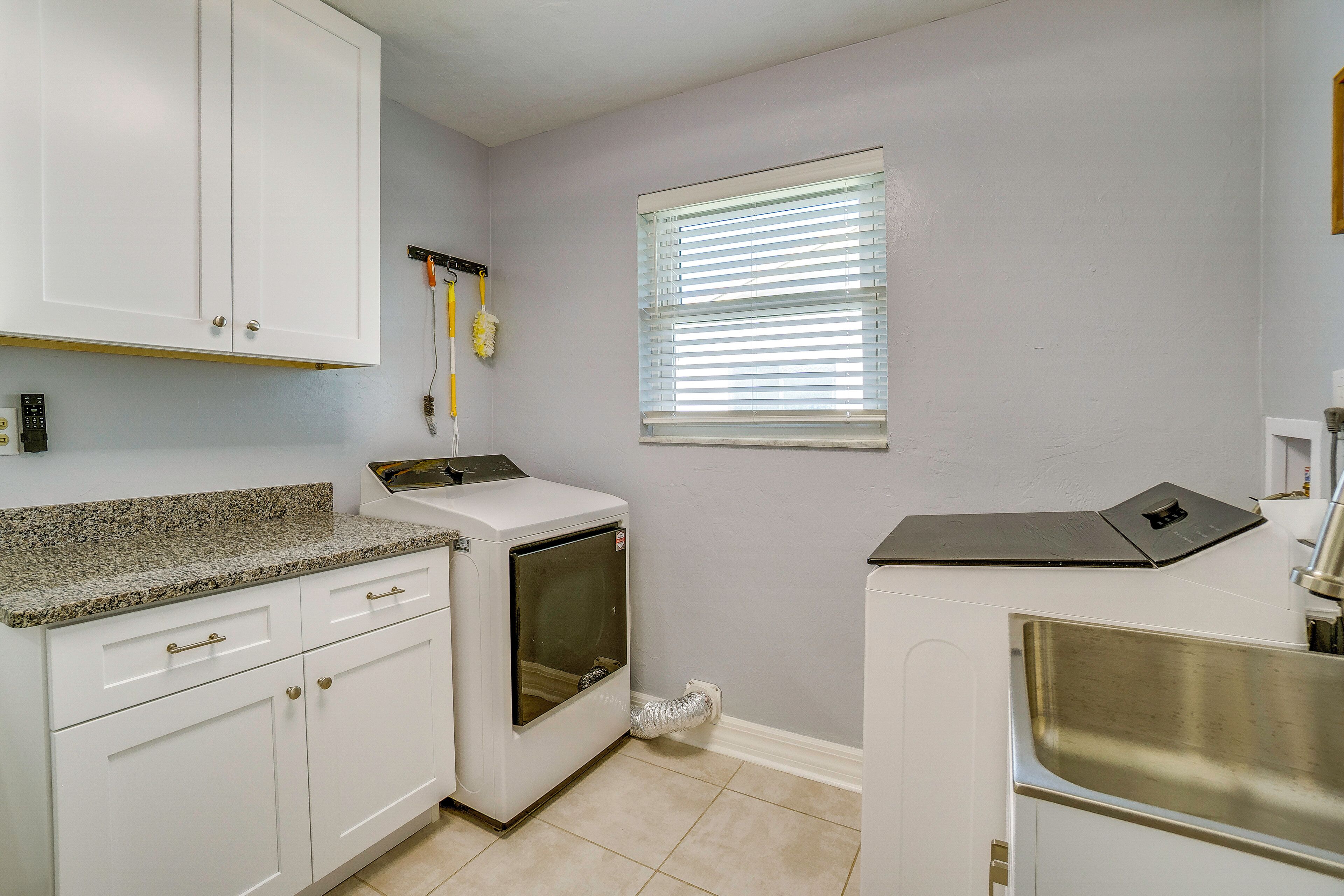 A kitchen with white cabinets, a built-in oven, a stainless steel sink, and a window with blinds.