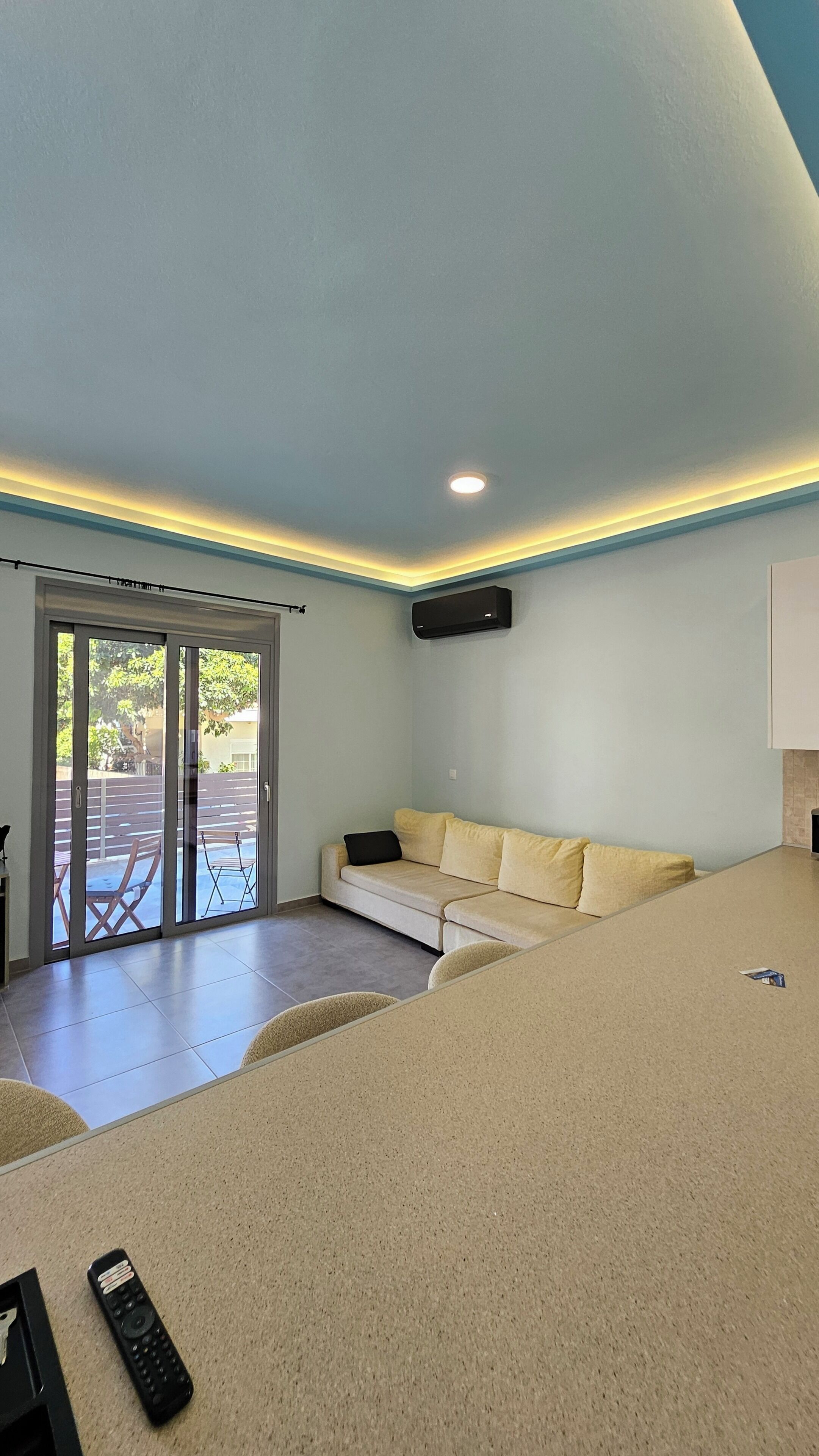 Una sala de estar con sofá, control remoto y puerta corrediza de vidrio que da a un área exterior.