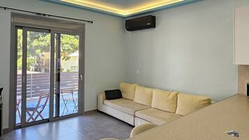 Una sala de estar con sofá, control remoto y puerta corrediza de vidrio que da a un área exterior.