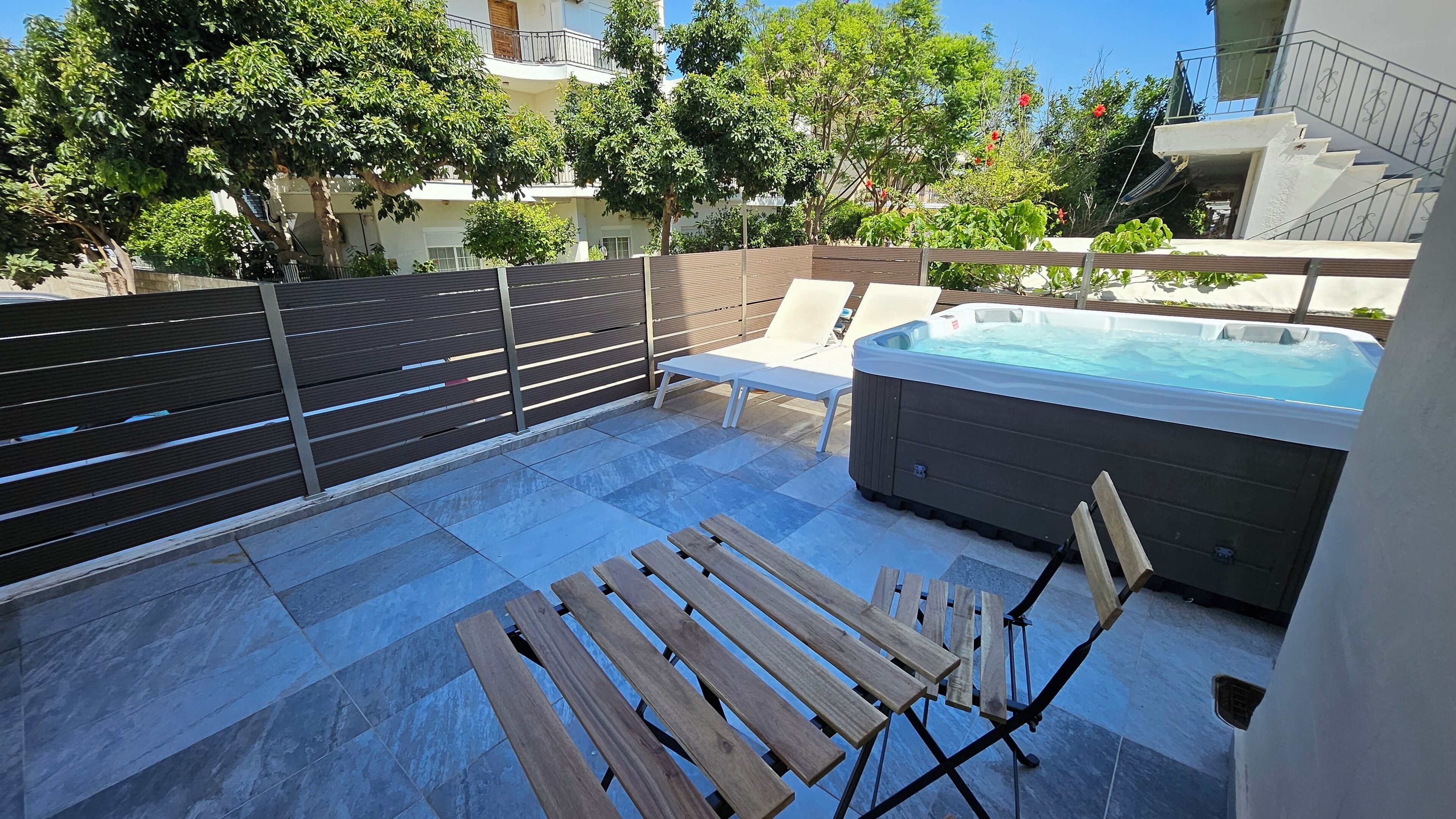 A patio with a hot tub, wooden benches, and a fence.