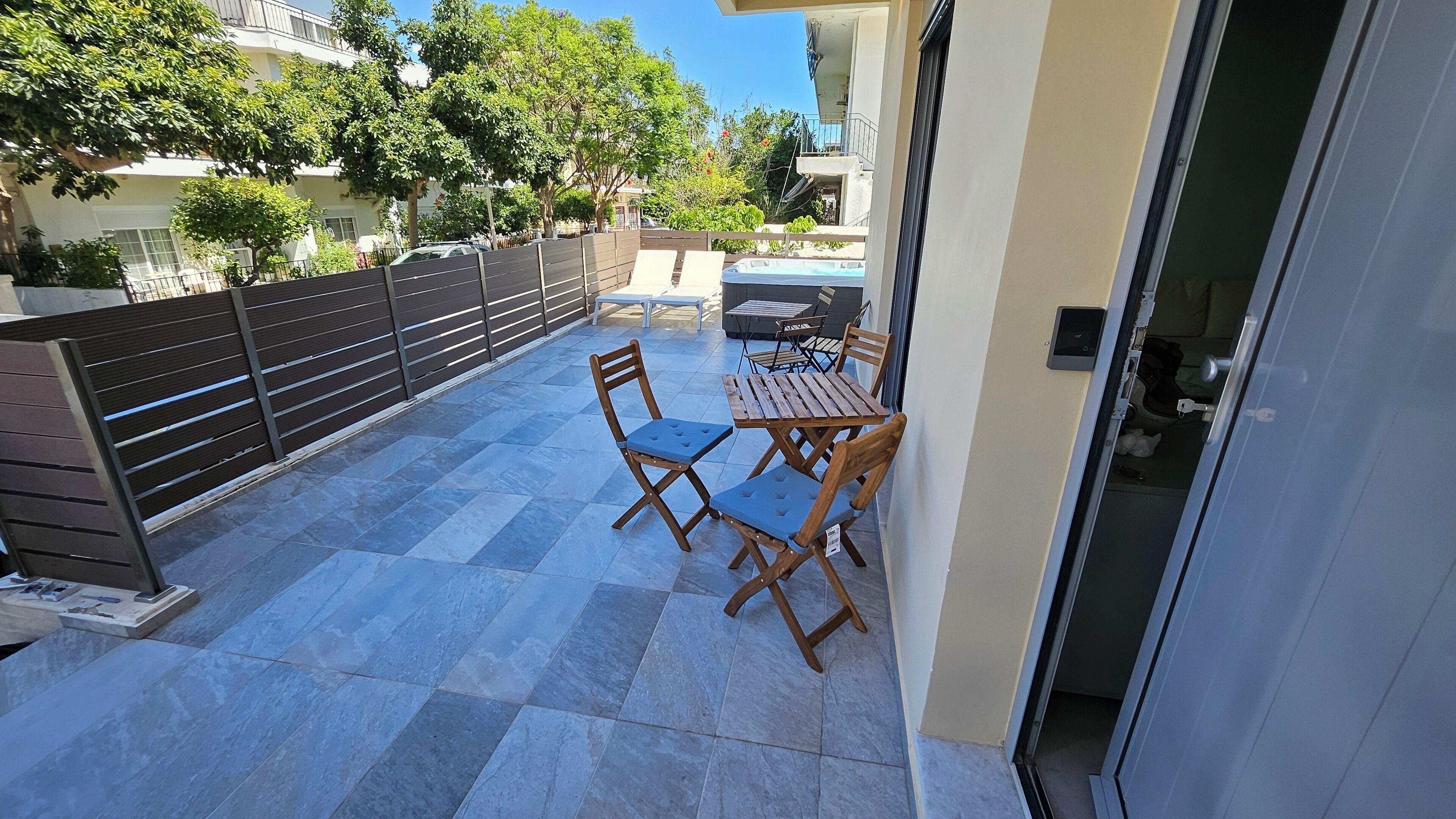 A balcony with a table and chairs, a hot tub, and a view of the surrounding buildings and trees.
