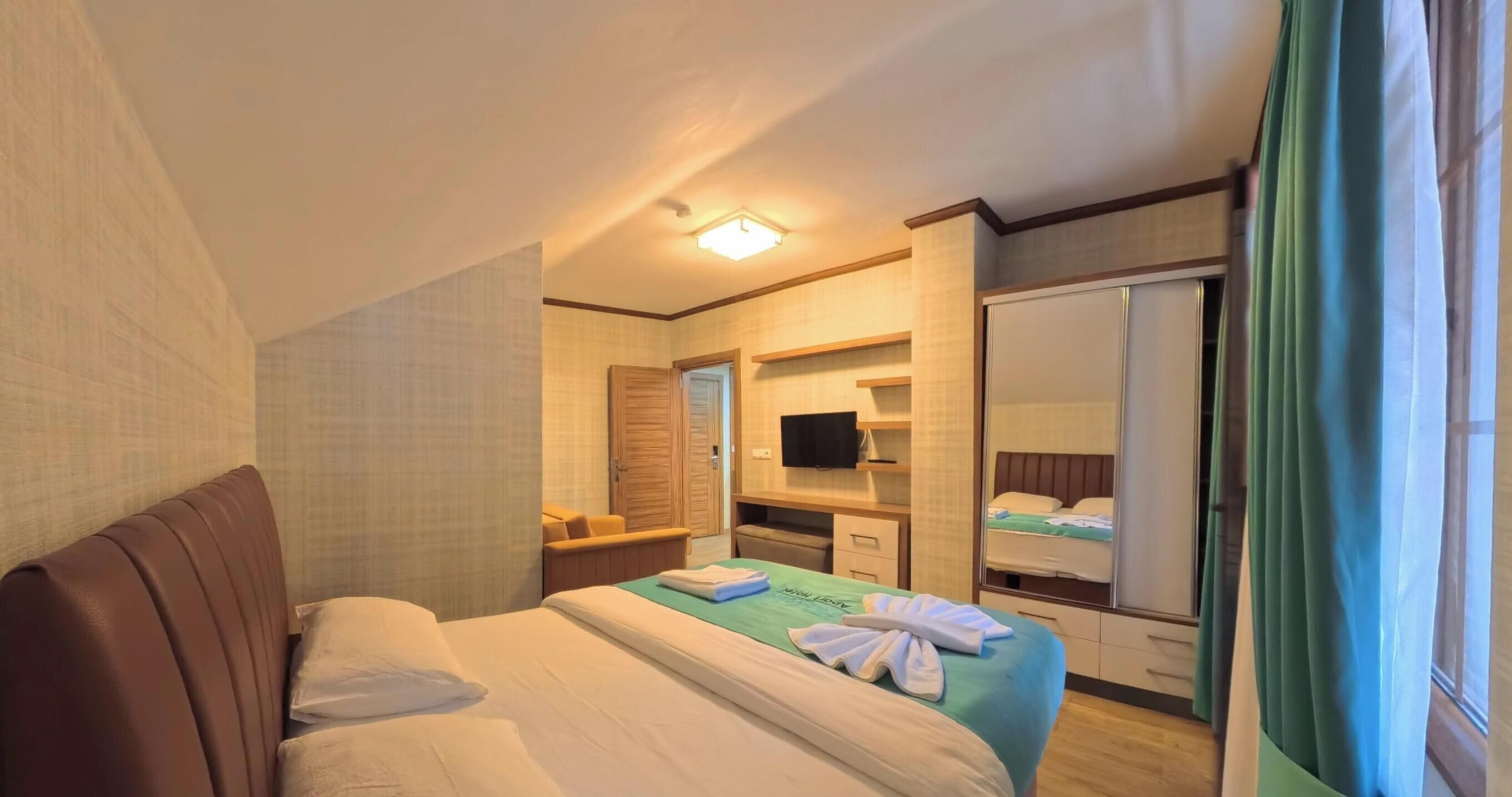 A hotel room with a bed, a television, a mirror, and a wardrobe.