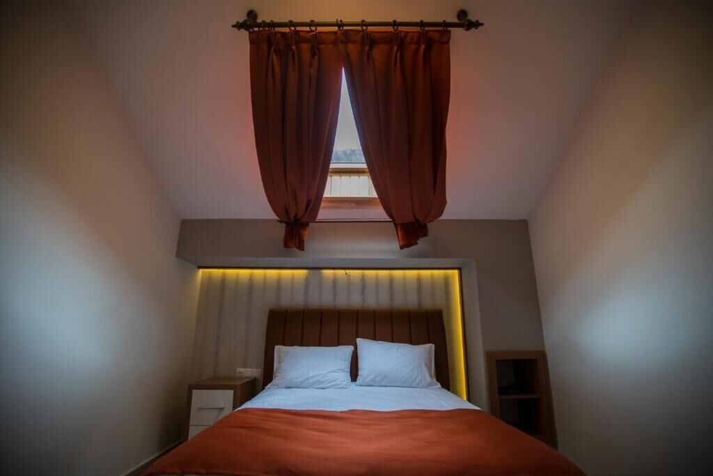 Un dormitorio con cama, mesita de noche y cortinas en la ventana.