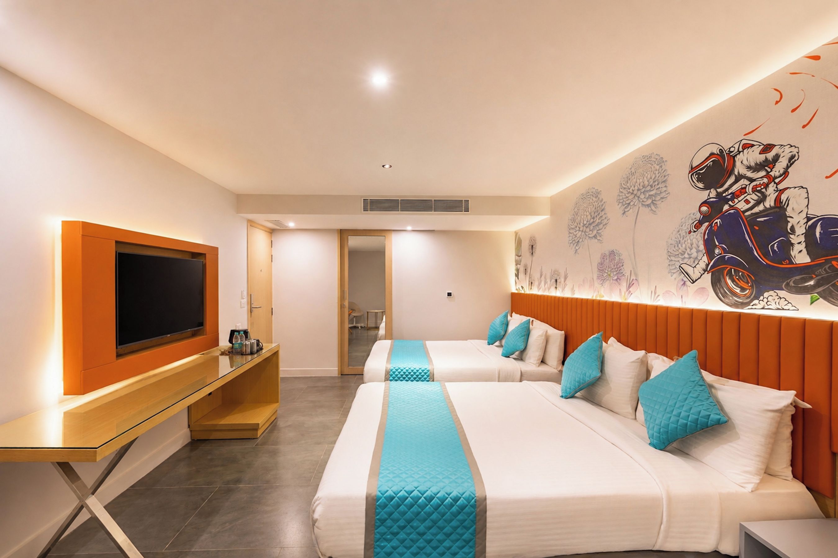 A hotel room with two beds, a TV, a desk, and a mural on the wall.