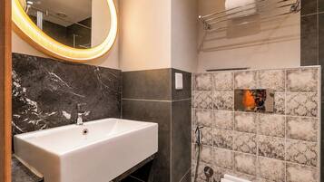 A bathroom with a white sink, a mirror with a light, and a shower area.