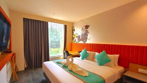 Quarto de hotel com uma cama grande, uma escrivaninha, televisão e vista para o verde lá fora.