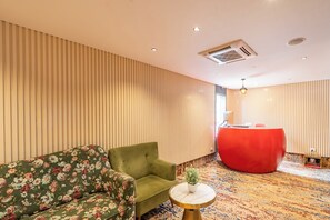 A room with a green sofa, a round table with a plant, and a red reception desk. - Neeladri Inn E-city (Doddathoguru)