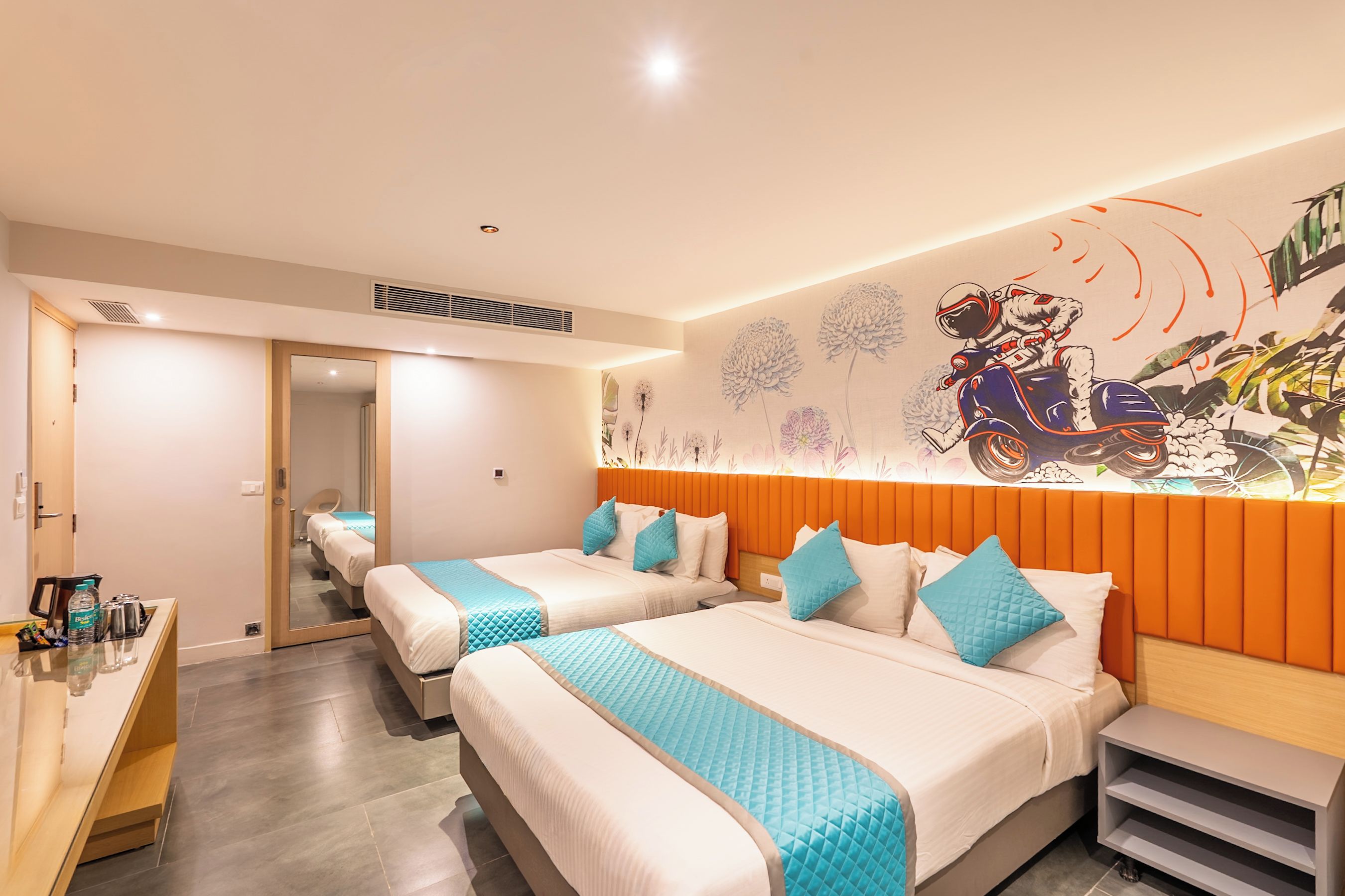 Habitación de hotel con dos camas, un escritorio y un mural en la pared.