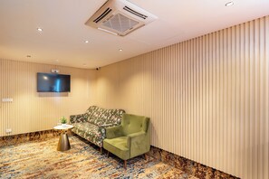A room with a sofa, a chair, a small table with a plant, a flat-screen TV mounted on the wall, and a patterned carpet. - Neeladri Inn E-city (Doddathoguru)