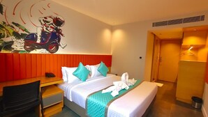 Quarto de hotel com duas camas, uma escrivaninha, uma cadeira, área de chuveiro e um mural na parede.