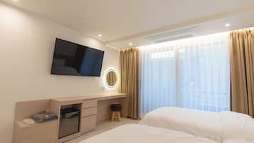 Ein Hotelzimmer mit einem Bett, einem an der Wand befestigten Fernseher, einem Schreibtisch mit Spiegel und einem Fenster mit Vorhängen.
