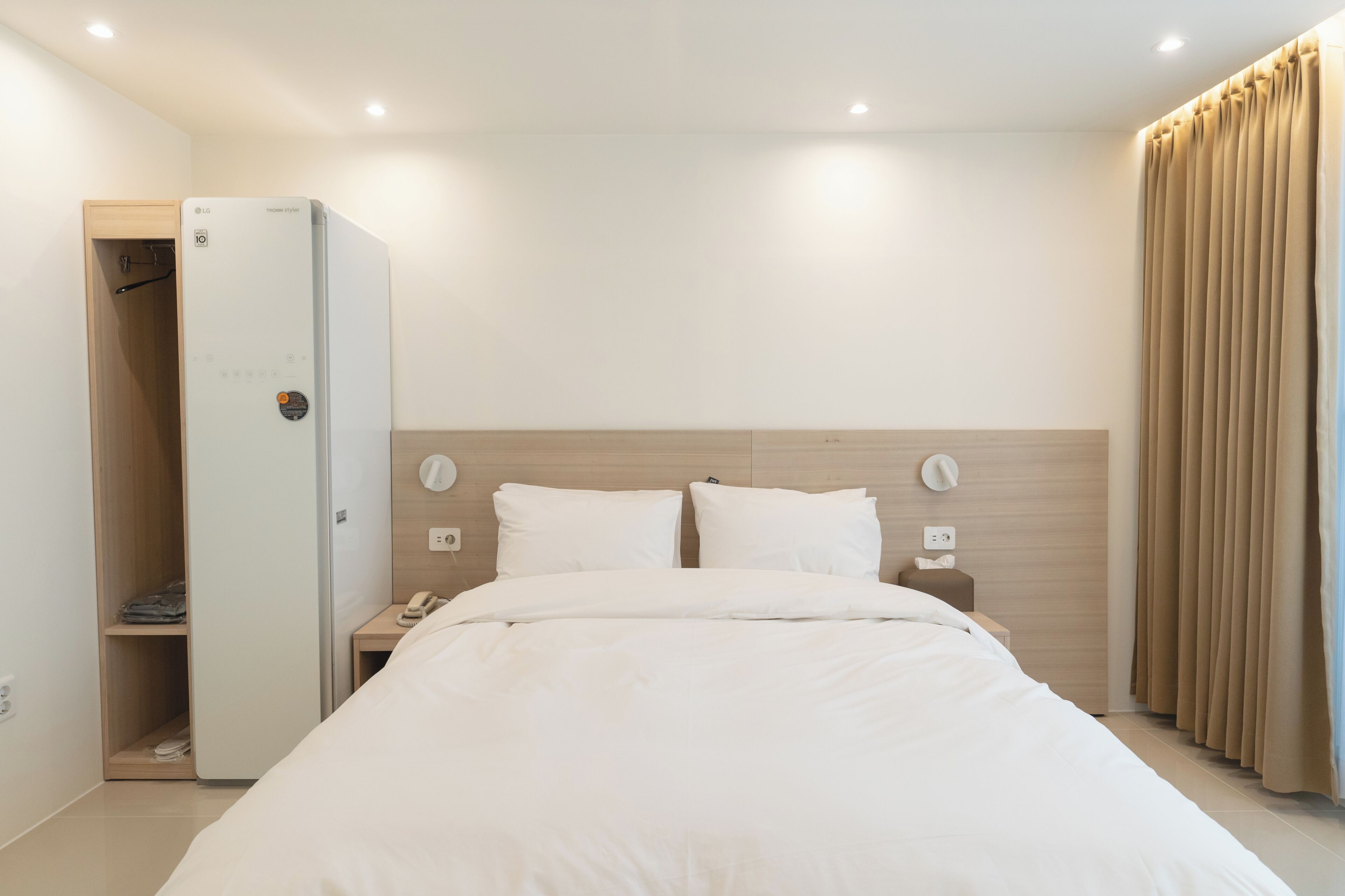 Habitación de hotel con cama, armario, mesita de noche, teléfono y cortina.