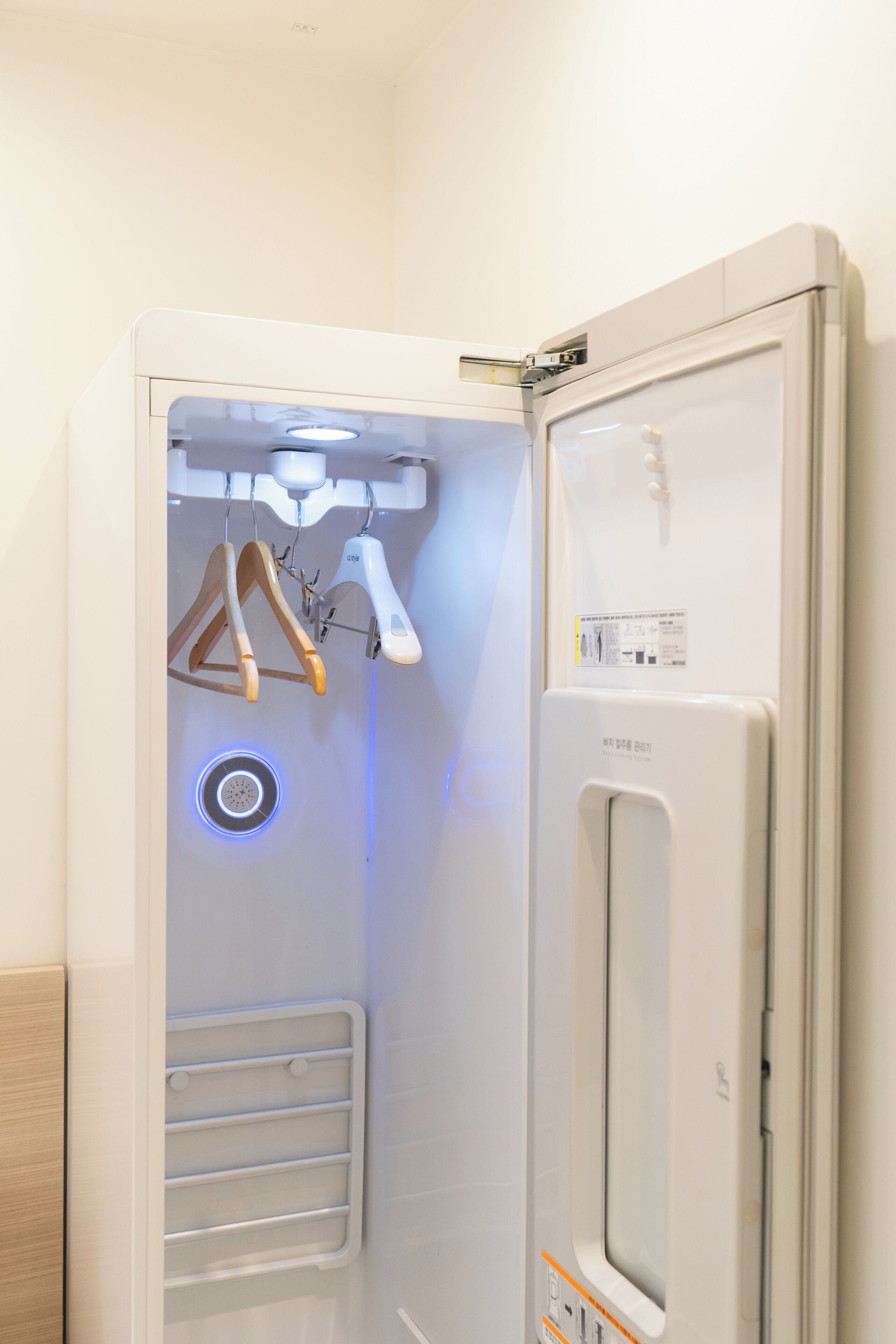 Habitación de hotel moderna con refrigerador integrado, un perchero de madera y una lámpara circular pequeña.