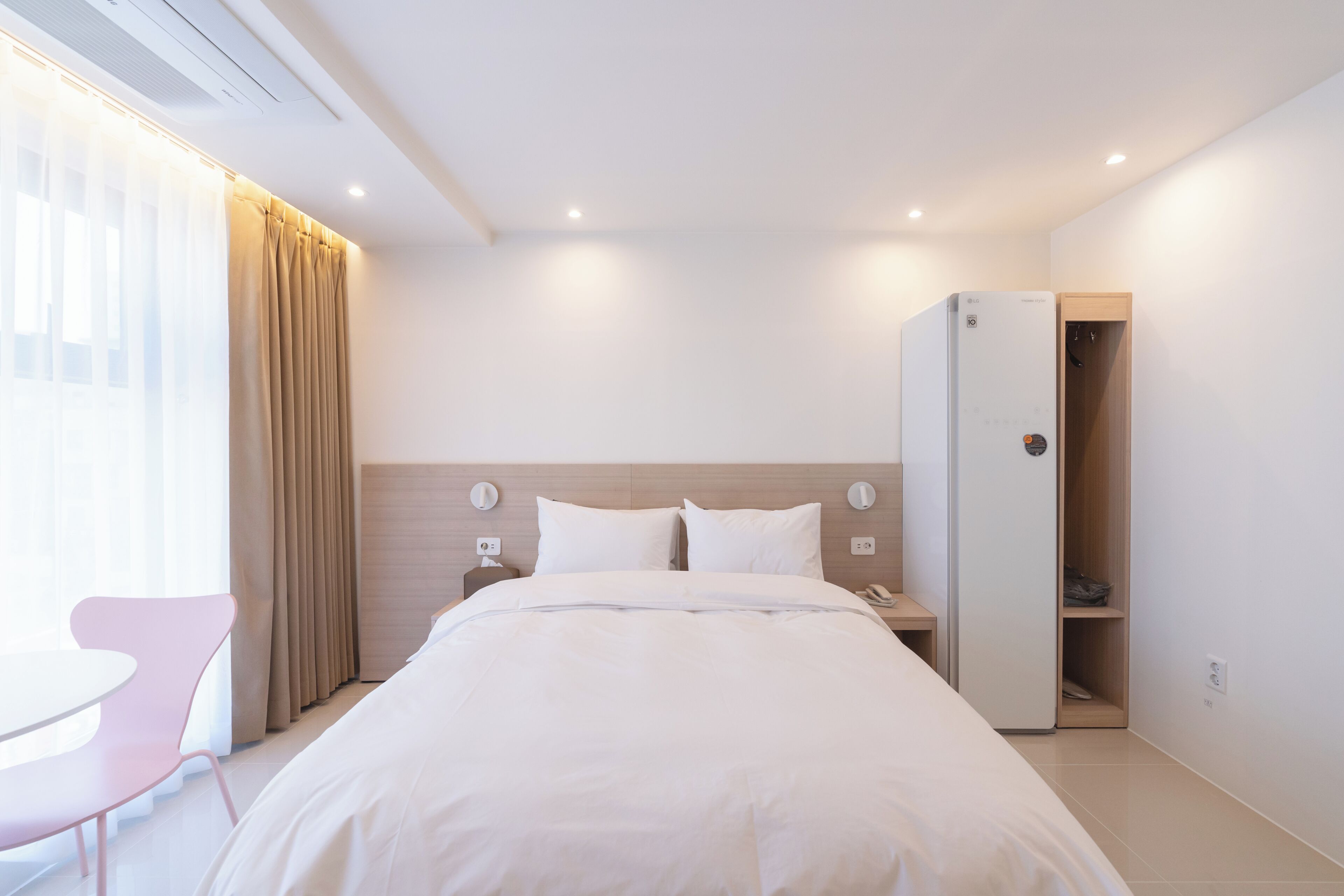 Ein Hotelzimmer mit Bett, Nachttisch, Stuhl, Kleiderschrank und einem fenster mit Vorhängen.
