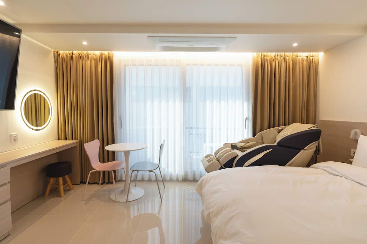 A hotel room with a bed, a desk with a chair, a round mirror, and a small table.
