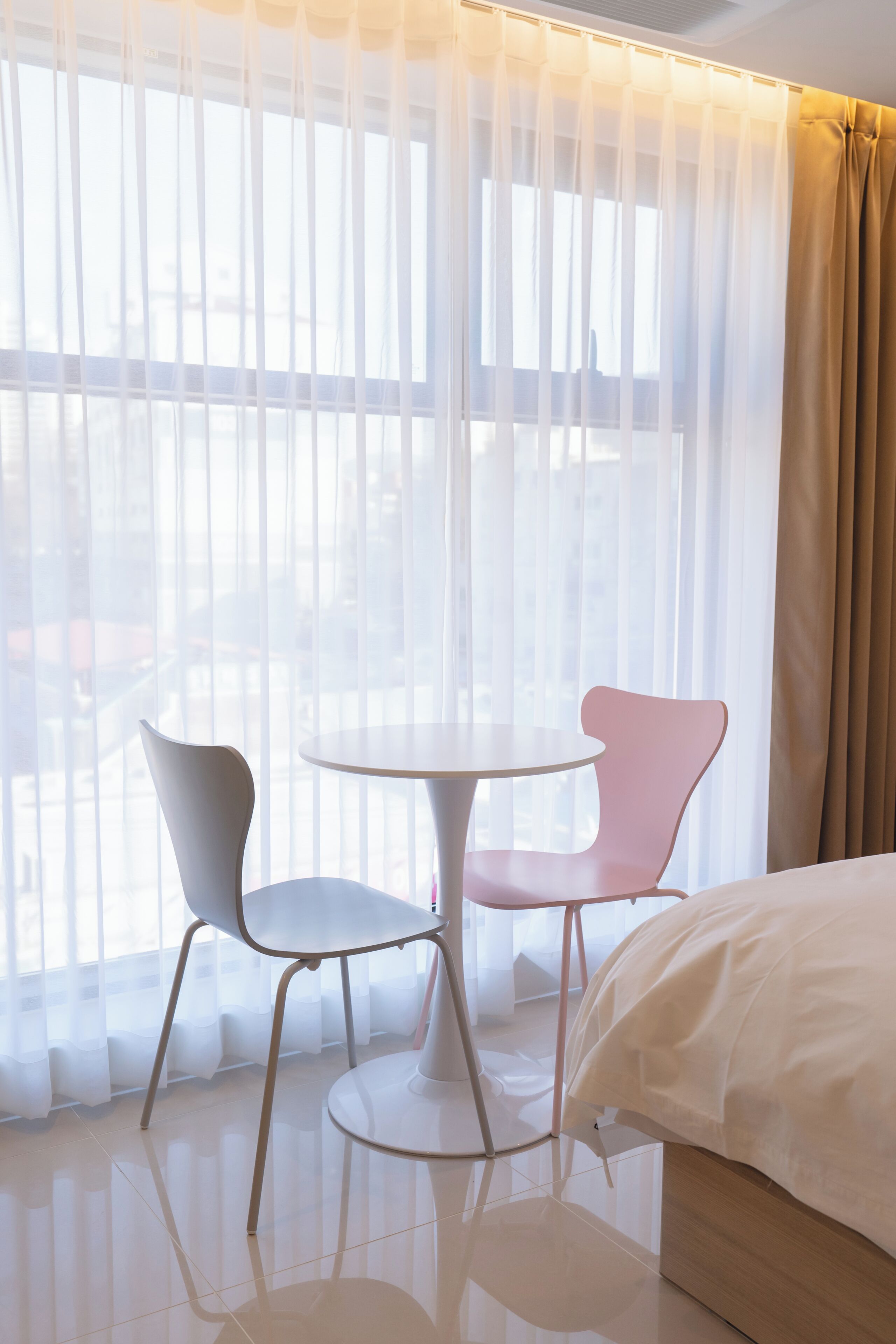 A hotel room with a bed, two chairs, a small round table, and sheer curtains.
