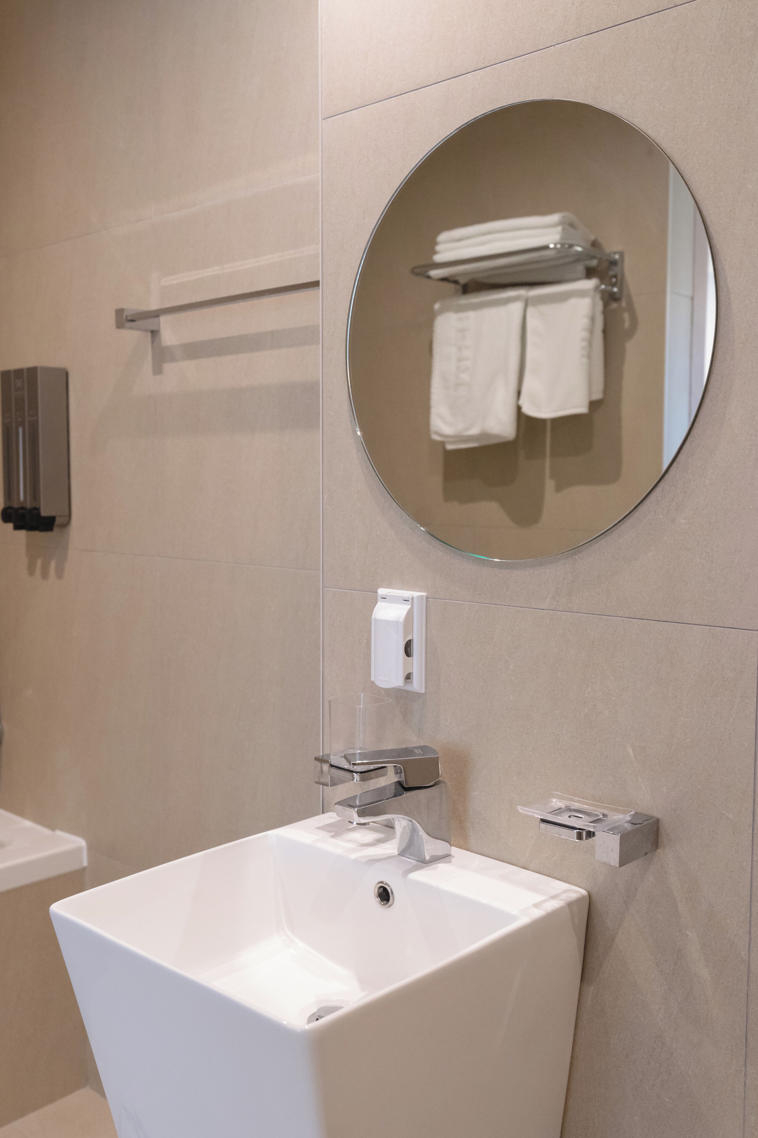 A bathroom with a white sink, a round mirror, and a towel rack.