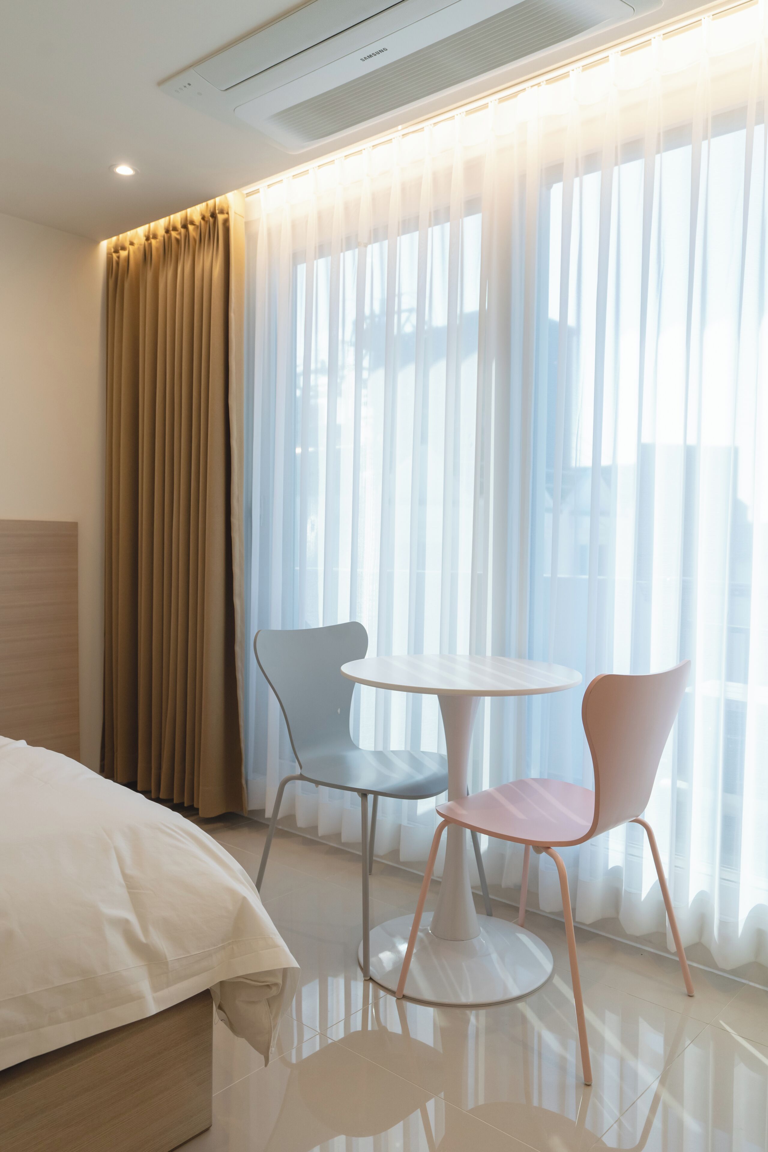 Ein Hotelzimmer mit einem Bett, zwei Stühlen, einem kleinen Tisch und durchsichtigen Vorhängen.
