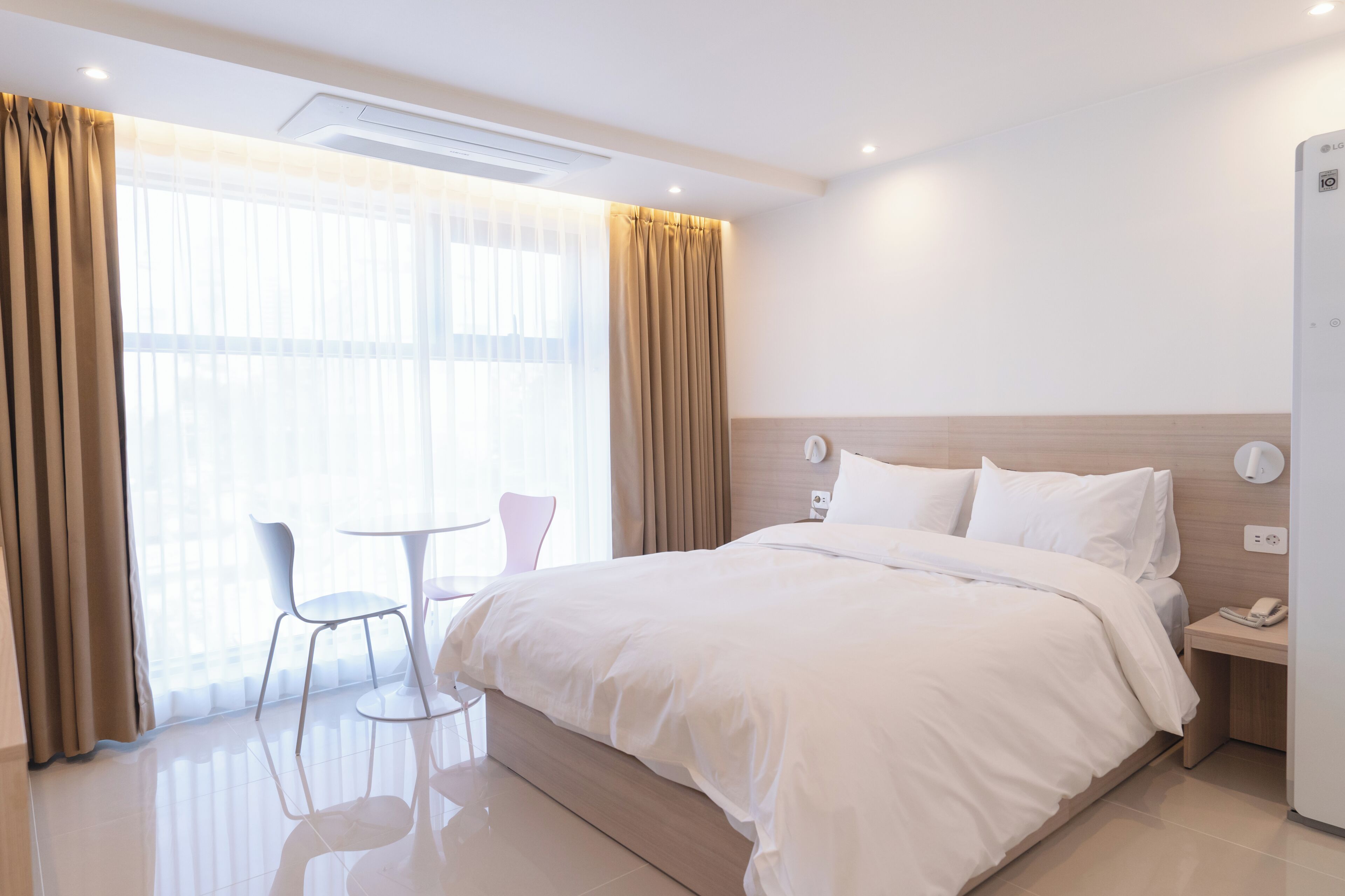 Una habitación de hotel con cama, mesita de noche, silla y una pequeña mesa.