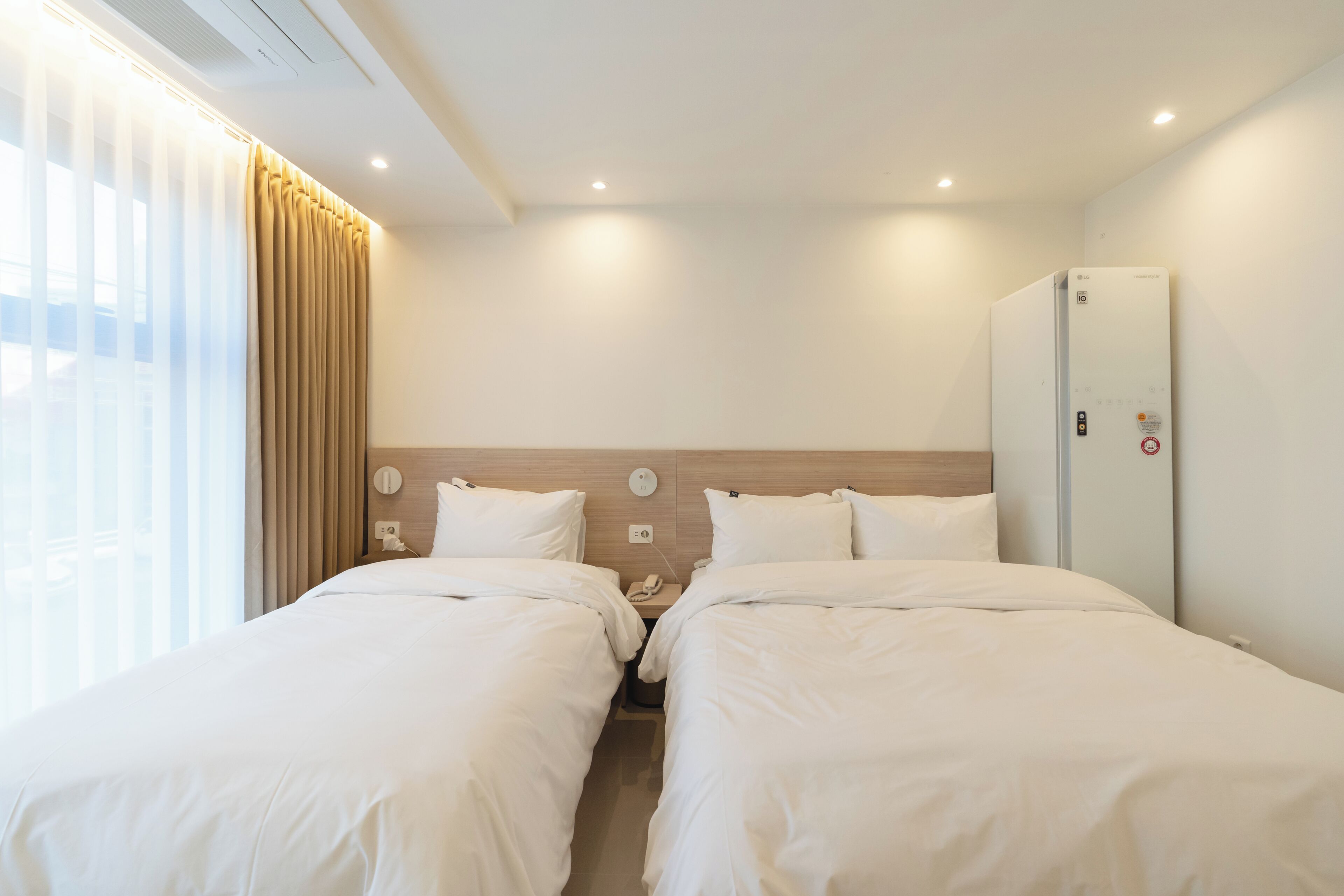 Habitación de hotel con dos camas, un armario, una mesita de noche con teléfono y una ventana con cortinas.