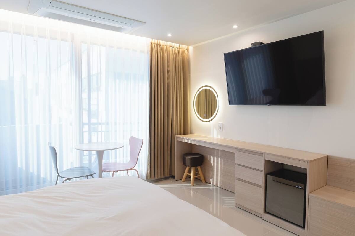A hotel room with a bed, a desk, a chair, a TV, and a window with curtains.