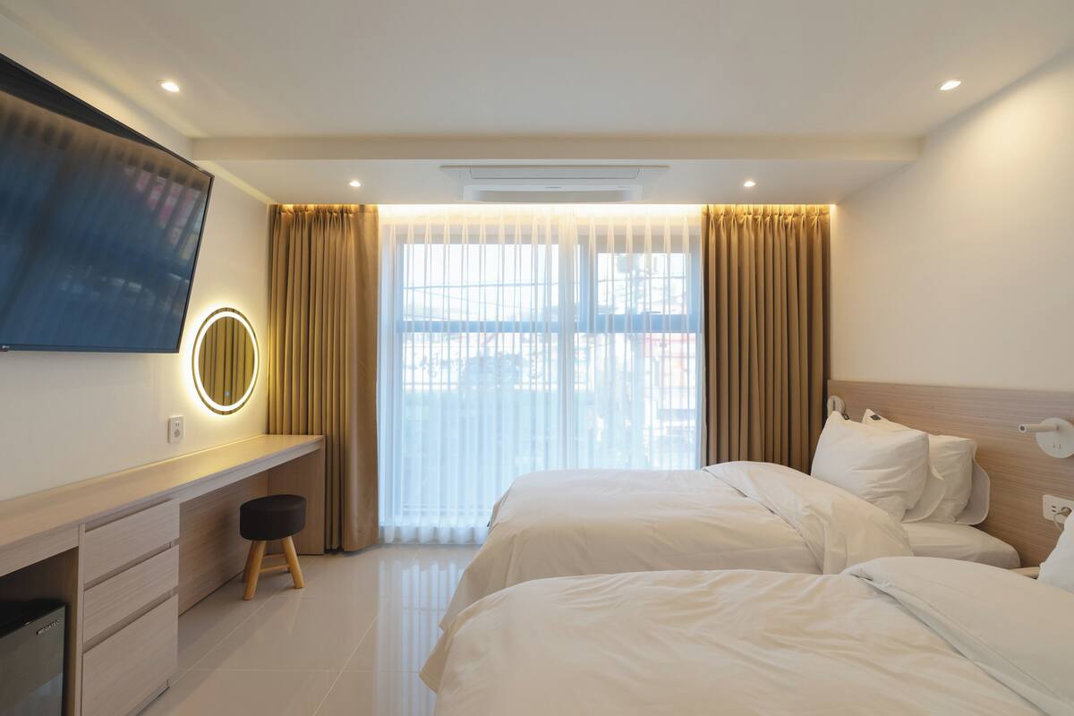 A hotel room with a bed, a desk with a chair, a television, and a window with curtains.