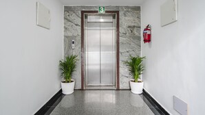 An elevator with a marble wall, two potted plants, and a fire extinguisher.