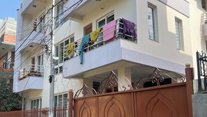 A multi-story residential building with balconies, a gated entrance, and a trash bin. - Central, Spacious Jawalakhel Hideaway on Quiet Residential Alley. (Lalitpur)