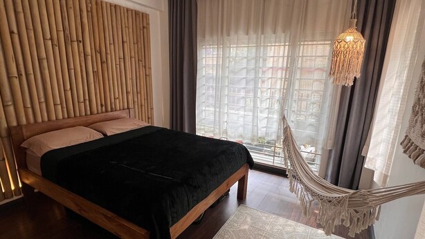 A bedroom with a wooden bed, a hanging chair, a patterned rug, and a window with curtains. - Central, Spacious Jawalakhel Hideaway on Quiet Residential Alley. (Lalitpur)