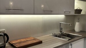 Uma cozinha moderna com armários brancos, uma pia de aço inoxidável e um tábua de corte de madeira.