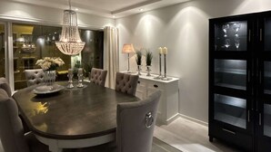 Uma sala de jantar moderna com uma mesa redonda, cadeiras estofadas, um candelabro e um aparador preto com portas de vidro.