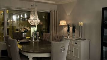 A dining area with a chandelier, cushioned chairs, a round table, and a sideboard with candles.