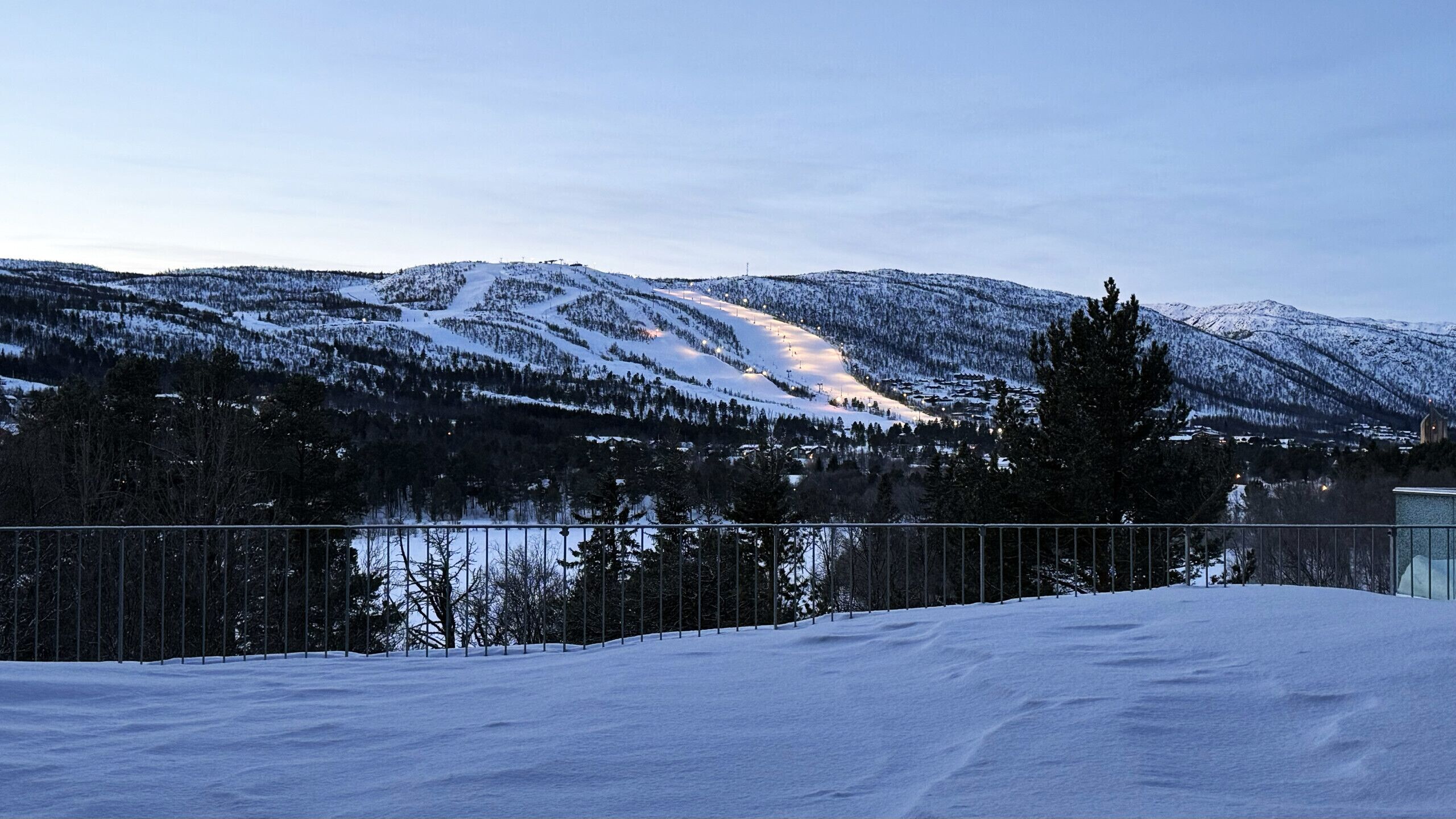 Ett snötäckt landskap med ett berg, en sjö och ett staket.