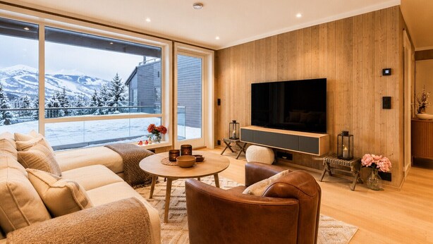 Un salon moderne doté d’un grand téléviseur, de sièges confortables, d’une cheminée et offrant une vue sur des montagnes enneigées.