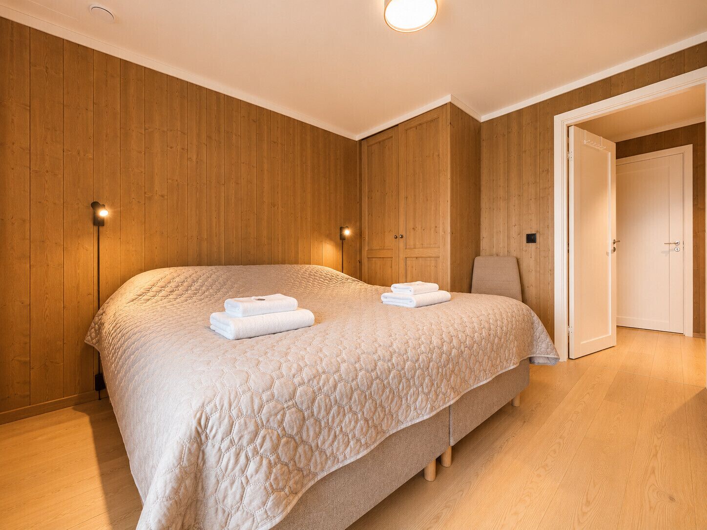 Un dormitorio con una cama grande, paredes de madera, una mesita de noche y una puerta.