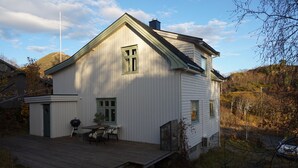 Une maison blanche avec une terrasse en bois, une cheminée et une antenne parabolique.