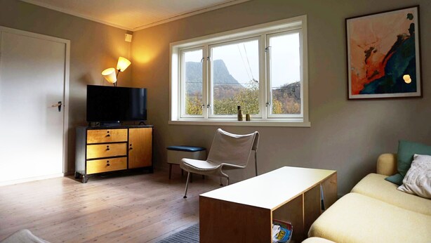 Une pièce avec un plancher en bois, un téléviseur posé sur un meuble, une chaise, une table, un lit, une fenêtre donnant sur un paysage et un tableau accroché au mur.