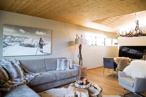 A cozy living room with a grey sofa, a fireplace, and a ski-themed artwork on the wall. - Alpine Retreat with Scenic Balcony (Neukirchen am Grossvenediger)