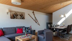 A modern living room with a sofa, armchair, coffee table, and dining area with chairs and a table. - Family Chalet Near Wildkogel Ski Slopes with Sauna (Neukirchen am Grossvenediger)