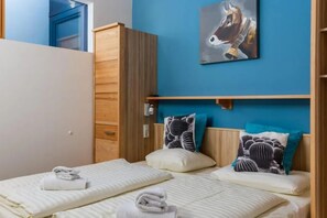 Une chambre avec deux lits, une armoire en bois, un mur bleu et un tableau représentant un cheval.