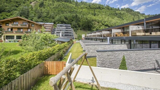 A modern hotel with a stone facade, a wooden deck, and a view of a forested hillside. - Family Chalet Near Wildkogel Ski Slopes with Sauna (Neukirchen am Grossvenediger)