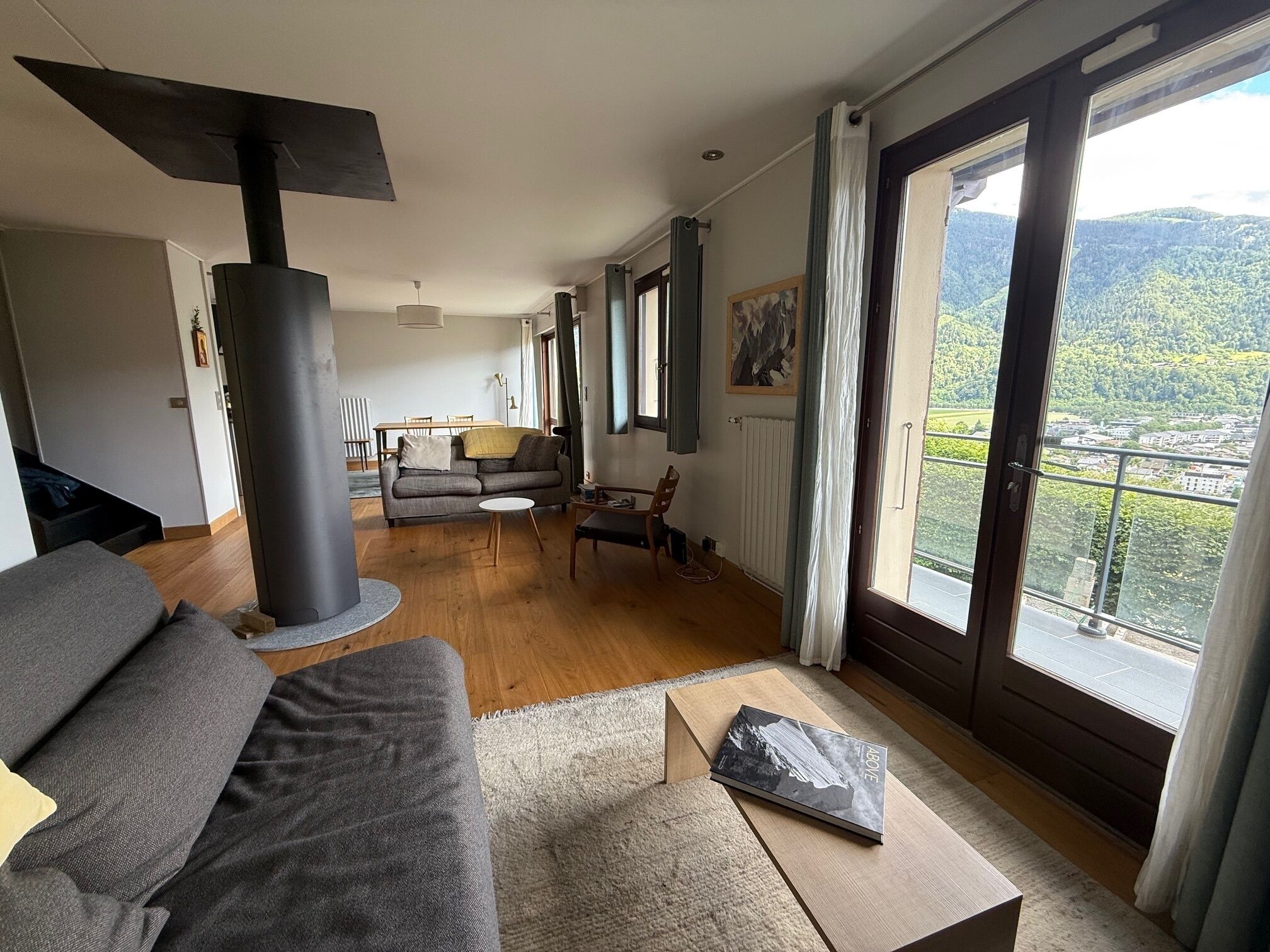 Una sala moderna con sofá, mesa de centro y chimenea. Hay un comedor con mesa y sillas, y ventanas grandes que ofrecen vistas al exterior.
