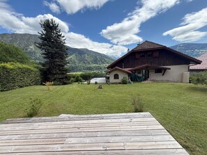 A wooden deck leading to a house with a sloped roof, surrounded by a well-maintained lawn and a mountain backdrop. - Chalet Mont Joly, mountain views, 20 minutes from Chamonix-Mont-Blanc (Passy)
