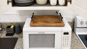 Una cocina con microondas integrado, tabla de cortar de madera, y diferentes platos y cristalería.